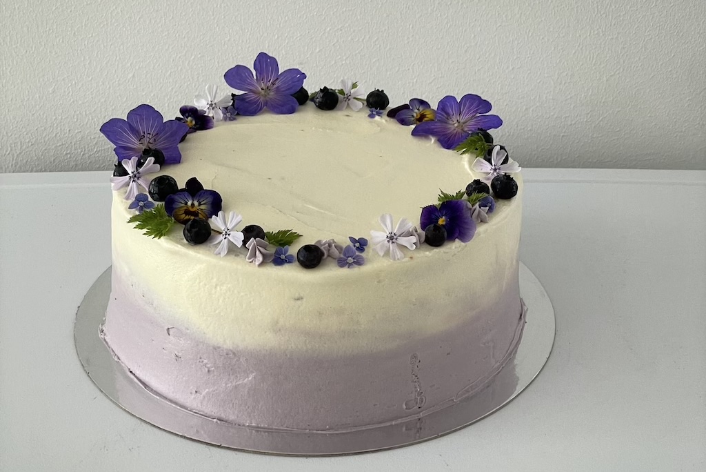 Violetti täytekakku aidoilla kukilla ja kermapursotuksilla.